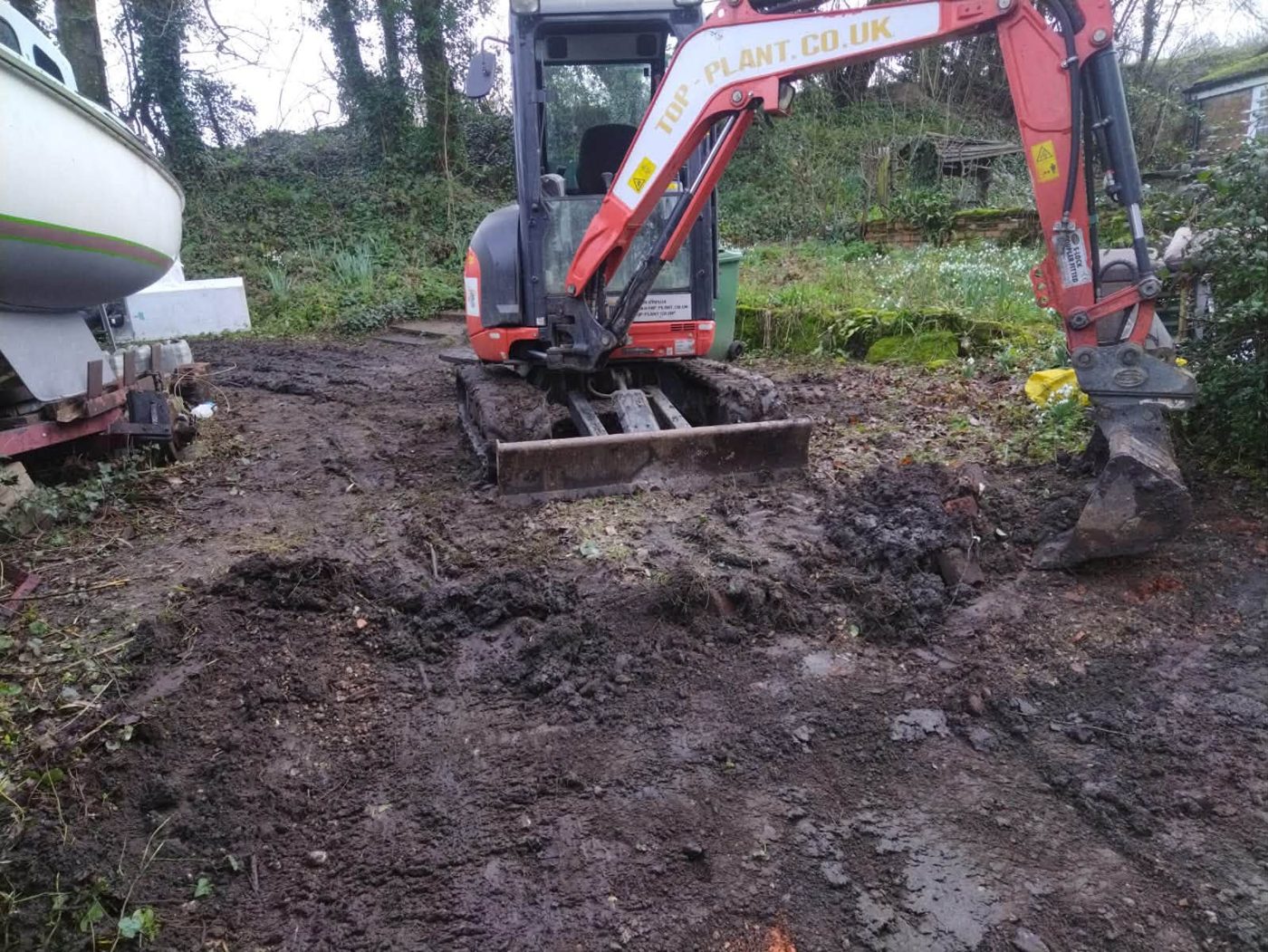 Mini digger clearing and levelling muddy ground
