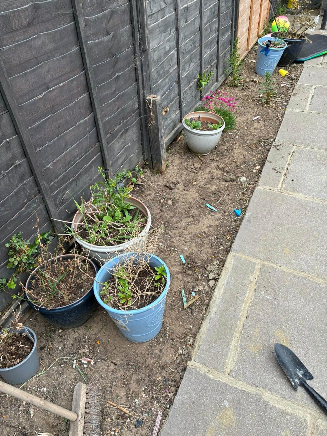 Cleared soil border with planters between a fence and a slab path
